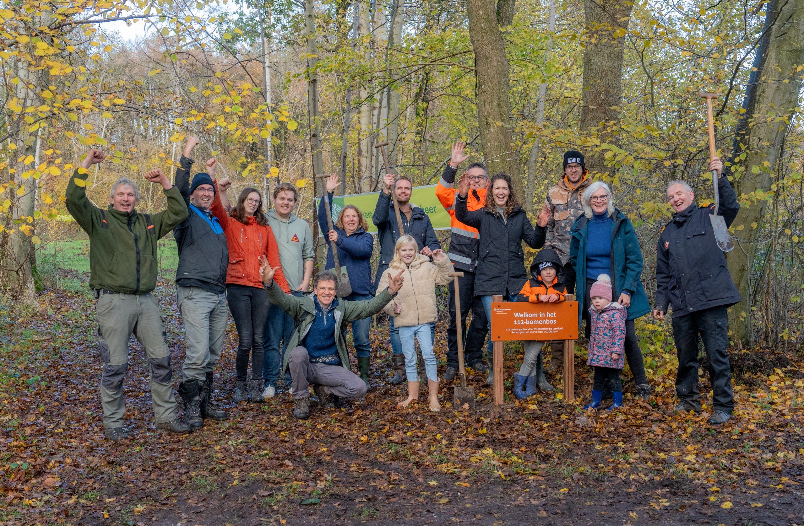 Groep mensen staan juichend, met een schop in de hand, bij het nieuwe bos.