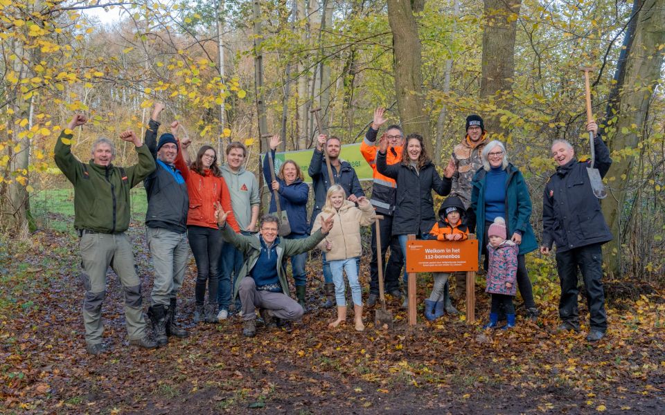 Groep mensen staan juichend, met een schop in de hand, bij het nieuwe bos.