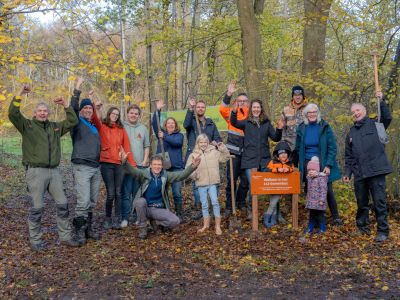 Groep mensen staan juichend, met een schop in de hand, bij het nieuwe bos.